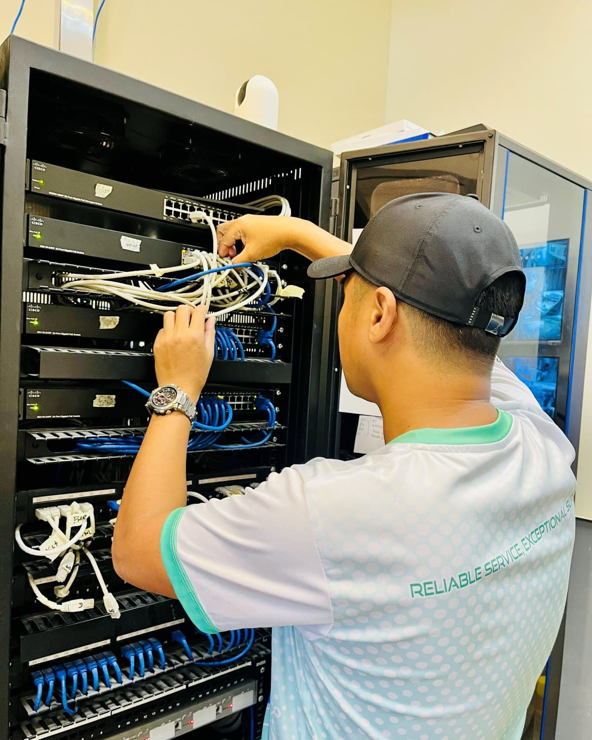 TechCare technician cabling a rack of Cisco switches and patch panels in a network room